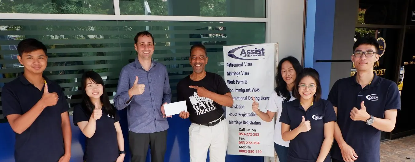 The Assist Thai Visa team in matching navy polo shirts, giving a thumbs up